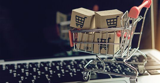 Bild mit kleinem Einkaufwagen vor Computer drauf zum Thema Onlineshopping