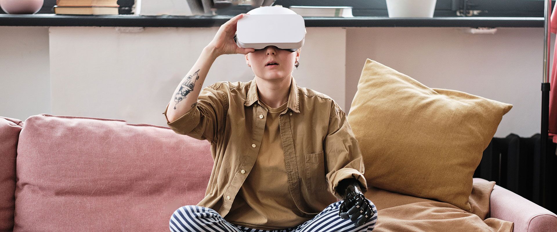 Jugendlicher Mensch mit Armprothese sitzt auf dem Sofa und nutzt eine VR-Brille